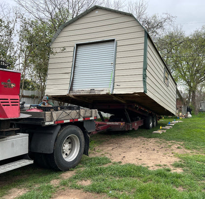 Small portable building being transported and unloaded from a flatbed truck in a residential area.