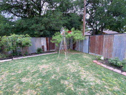 Backyard alteration with rustic barn tin installed to chain link fence for privacy with a windmill, grass, and trees after picture