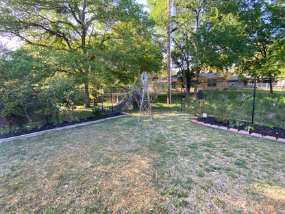 Backyard with grass, trees, and a windmill on a sunny day. Neighbor houses in plain view. before pic