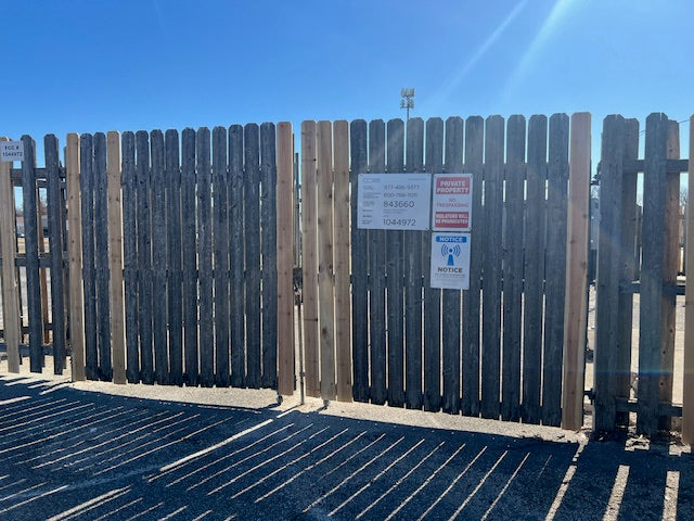 A wooden fence with new pickets guide wheel and a 'No Trespassing' sign attached to it, indicating the boundary of a property.