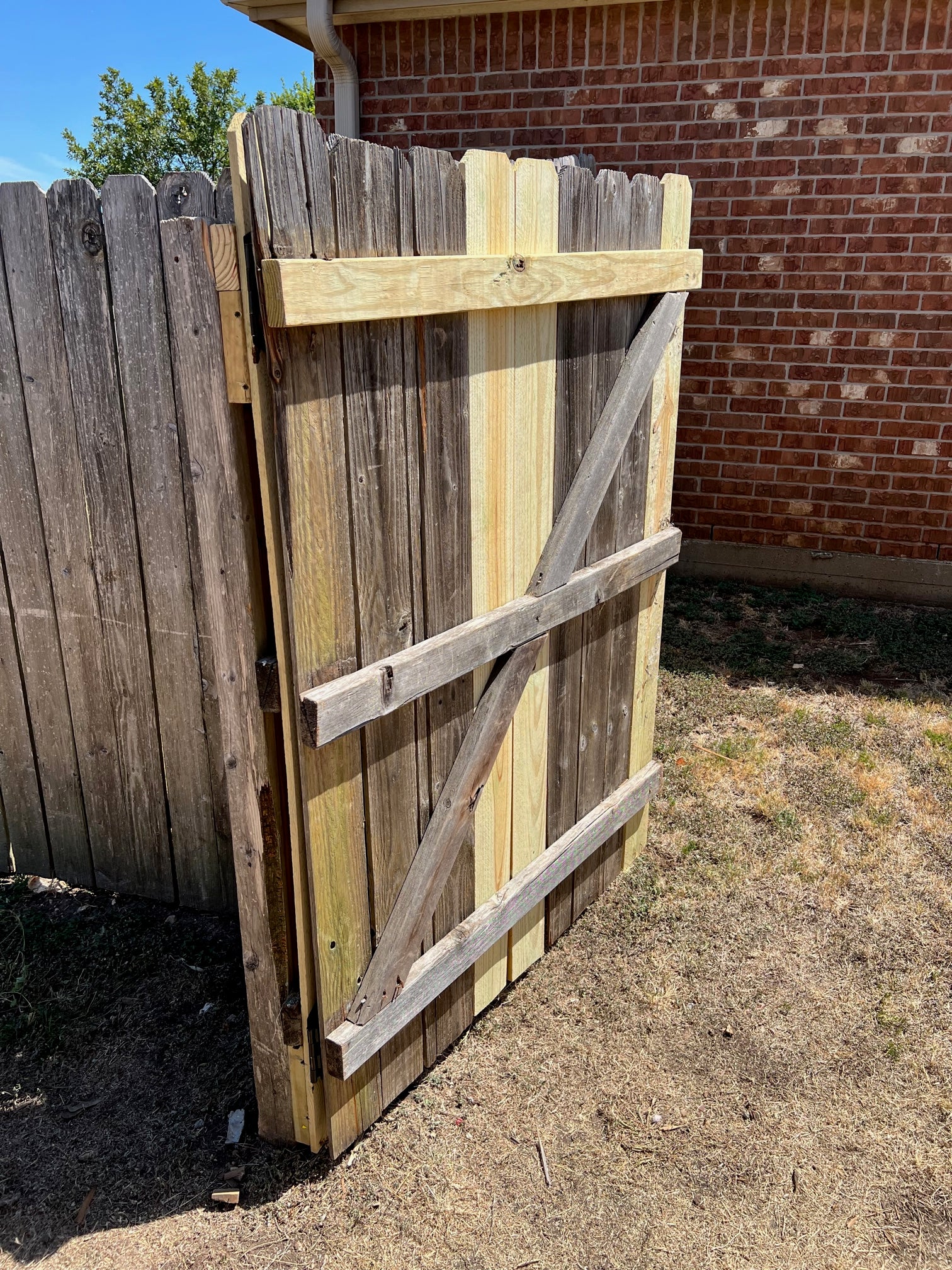 Privacy fence gate repaired and standing open to show the replaced bracing and functional hinge operation