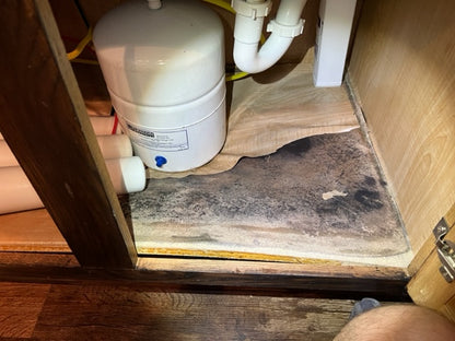 Water filter under a wooden cabinet with visible mold on the floor. Before picture.