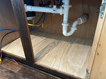 Inside a home kitchen cabinet with visible plumbing pipes wires and new wood. After picture.