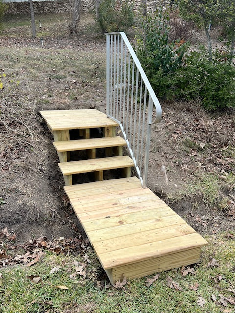 Replaced treated lumber wooden staircase and mini deck with metal handrail on a grassy and leaf-covered ground.