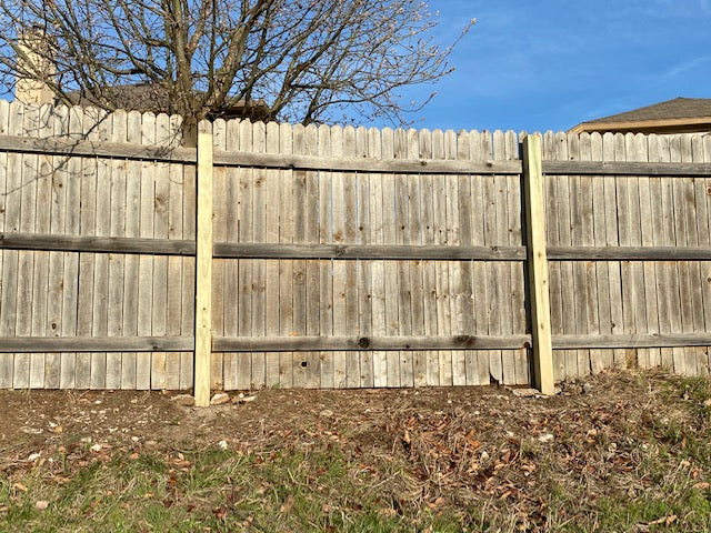 Repaired privacy fence showing two replaced four by four posts with concrete.