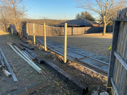 Wooden framing materials on the ground with a wooden fence and trees in the background while post are being replaced during picuture