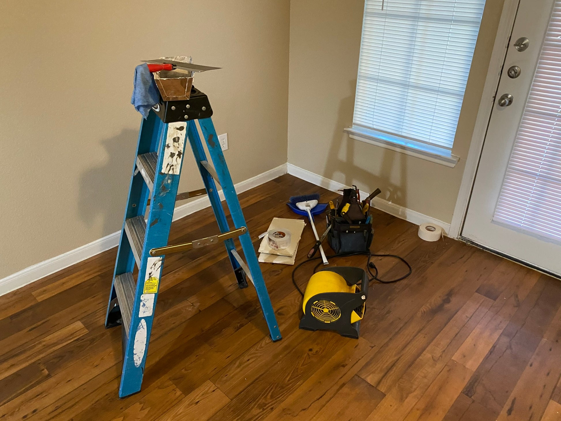 Blue ladder on a wooden floor with tools and equipment in a room.